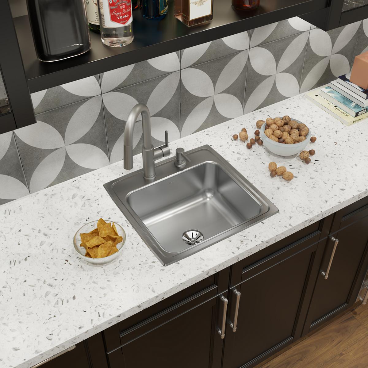Stainless steel drop-in sink with single bowl and brushed faucet installed in white speckled countertop.