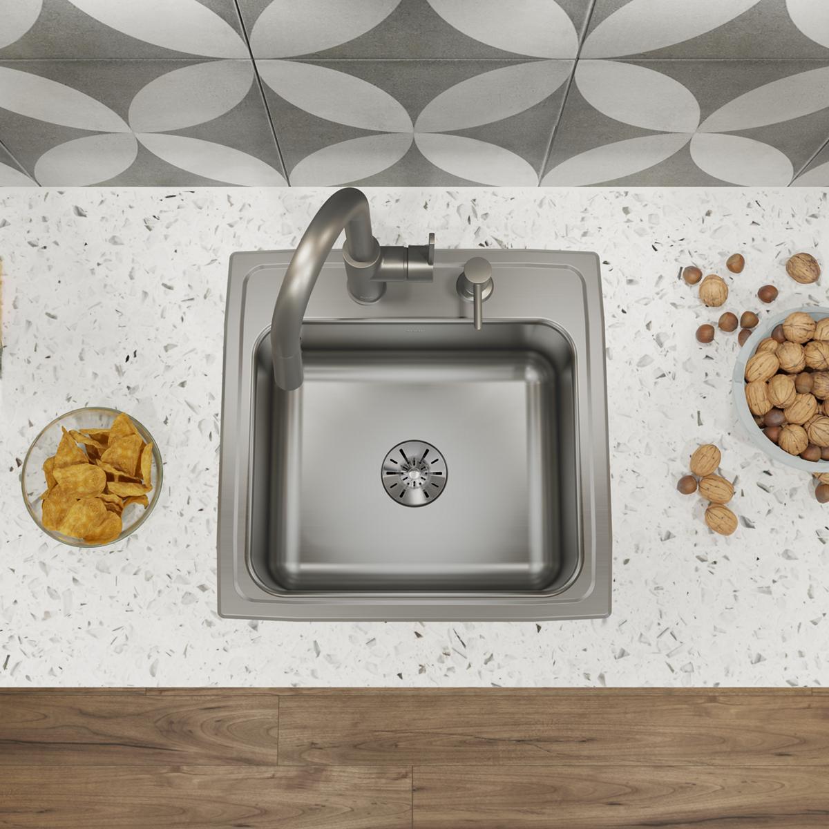 Stainless steel drop-in sink with single bowl, two faucet holes, and drain visible from above, installed in white speckled co
