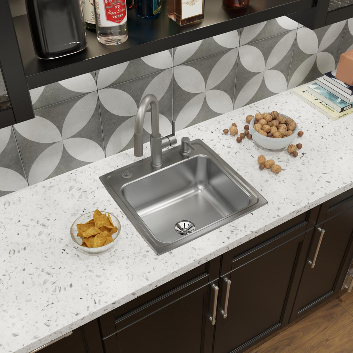 Stainless steel single bowl drop-in sink with three holes and matching faucet installed in white quartz countertop.