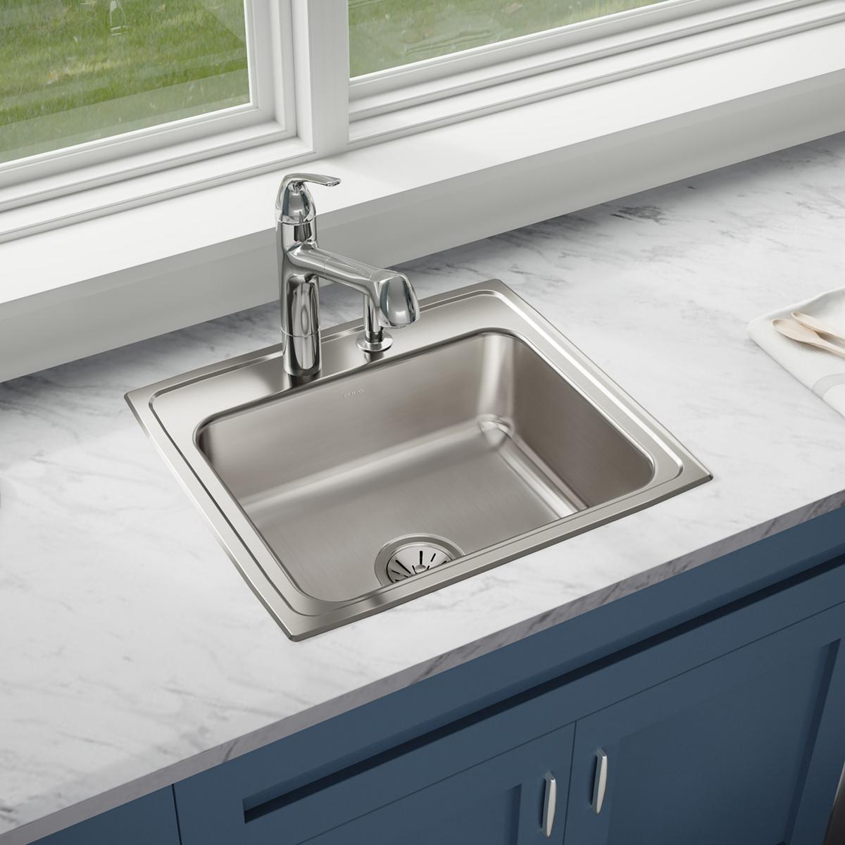 Stainless steel single bowl drop-in sink with chrome faucet installed in marble countertop with blue cabinetry below.