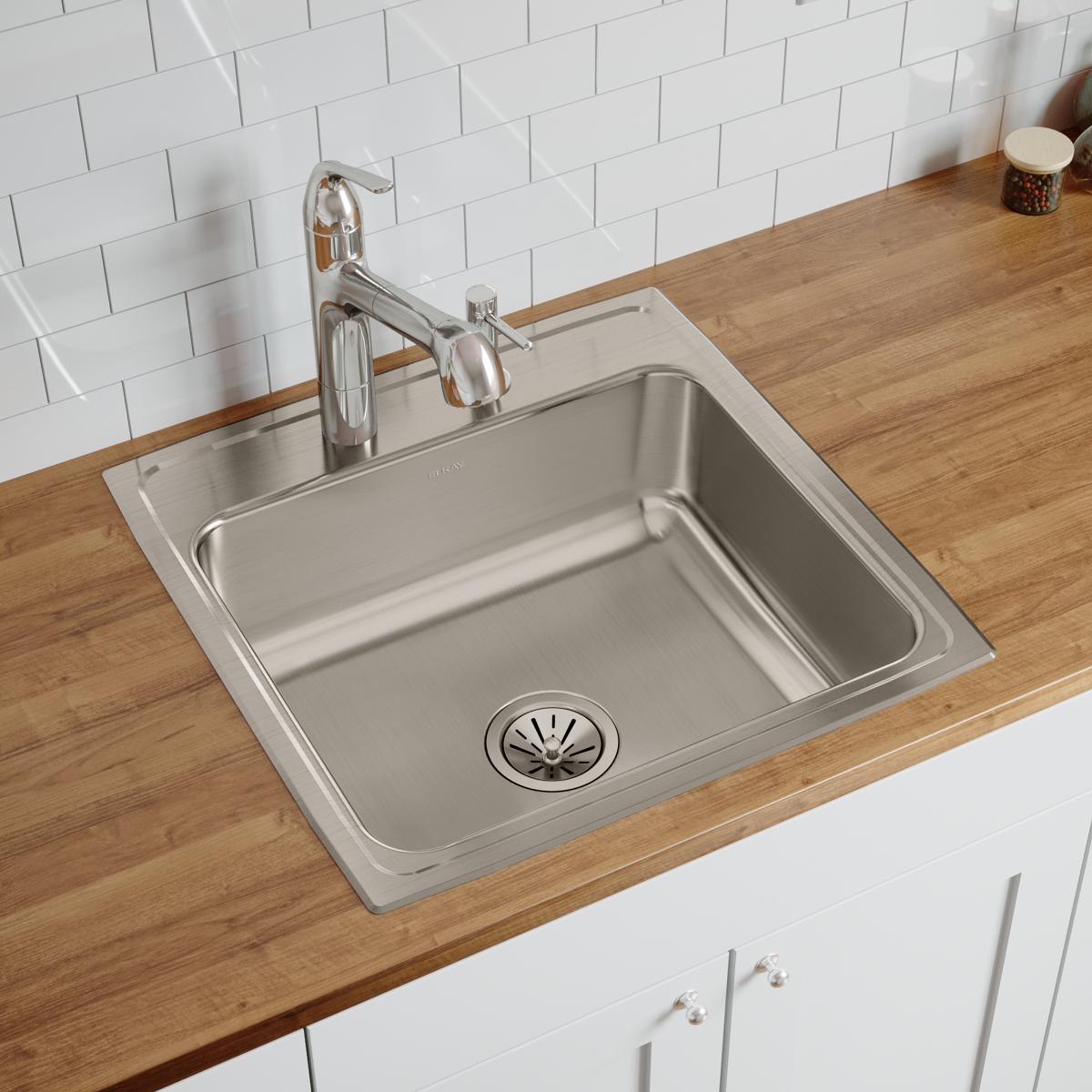 Stainless steel single bowl drop-in sink with drain installed in wood countertop, chrome faucet and white subway tile backspl
