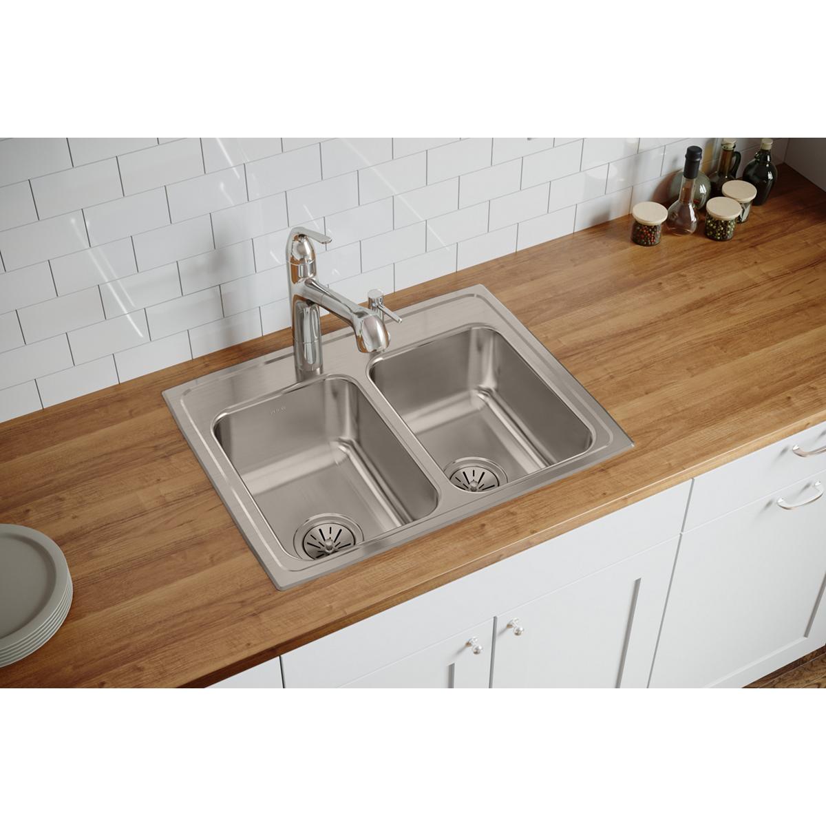 Stainless steel double bowl drop-in sink with two faucet holes, installed in wood countertop with white subway tile backsplas