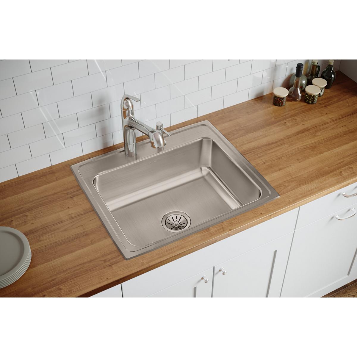 Stainless steel drop-in sink with single bowl and two faucet holes installed in wood countertop with white subway tile backsp