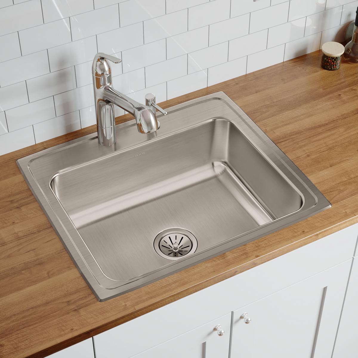 Stainless steel single bowl drop-in sink with two faucet holes installed in wood countertop with white subway tile backsplash
