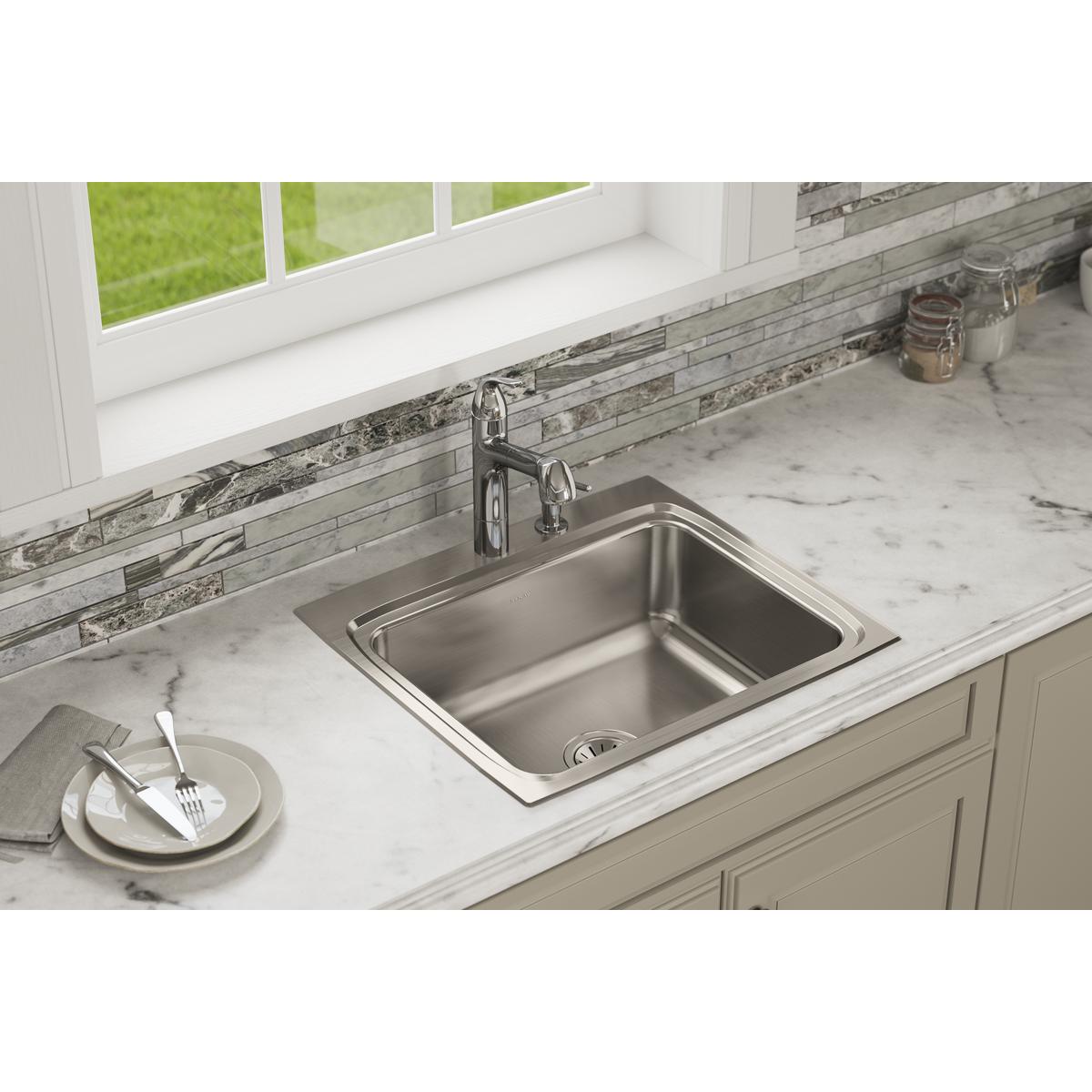 Stainless steel single bowl drop-in sink installed in marble countertop with faucet and drain visible.