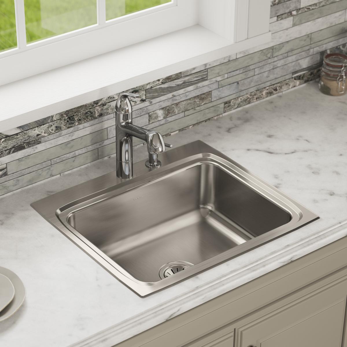 Stainless steel drop-in sink with single bowl and one faucet hole installed in white countertop.
