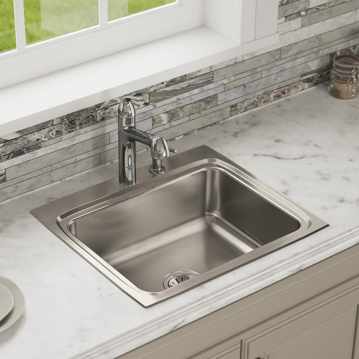 Stainless steel drop-in sink with single bowl and two faucet holes installed in marble countertop with tile backsplash.