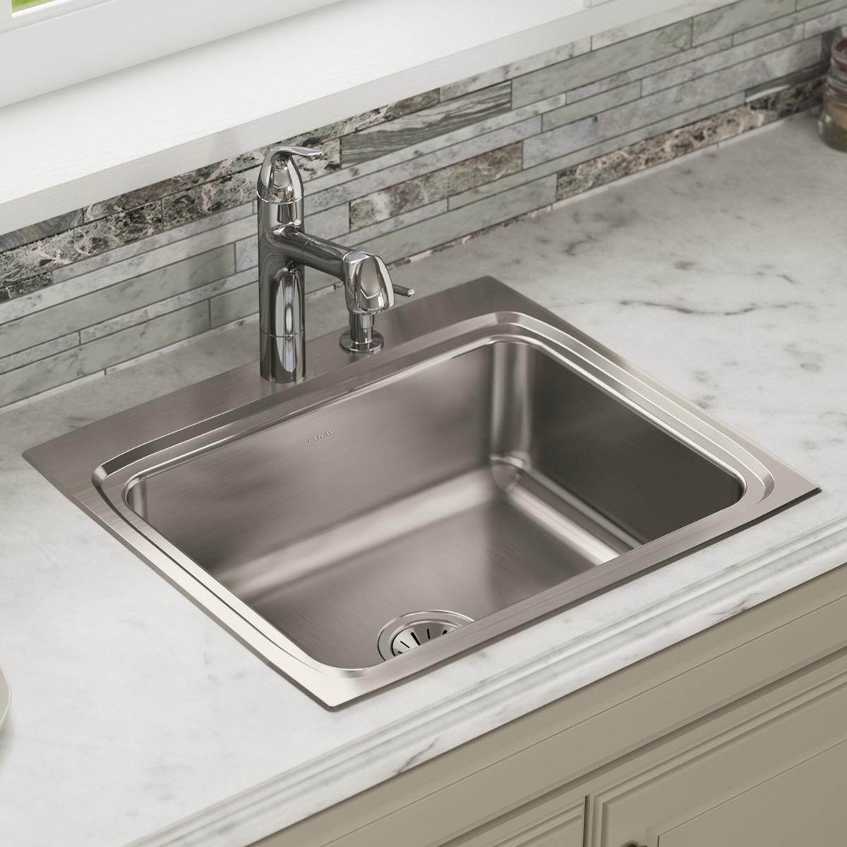 Stainless steel single bowl drop-in sink with polished finish and chrome faucet installed in marble countertop.