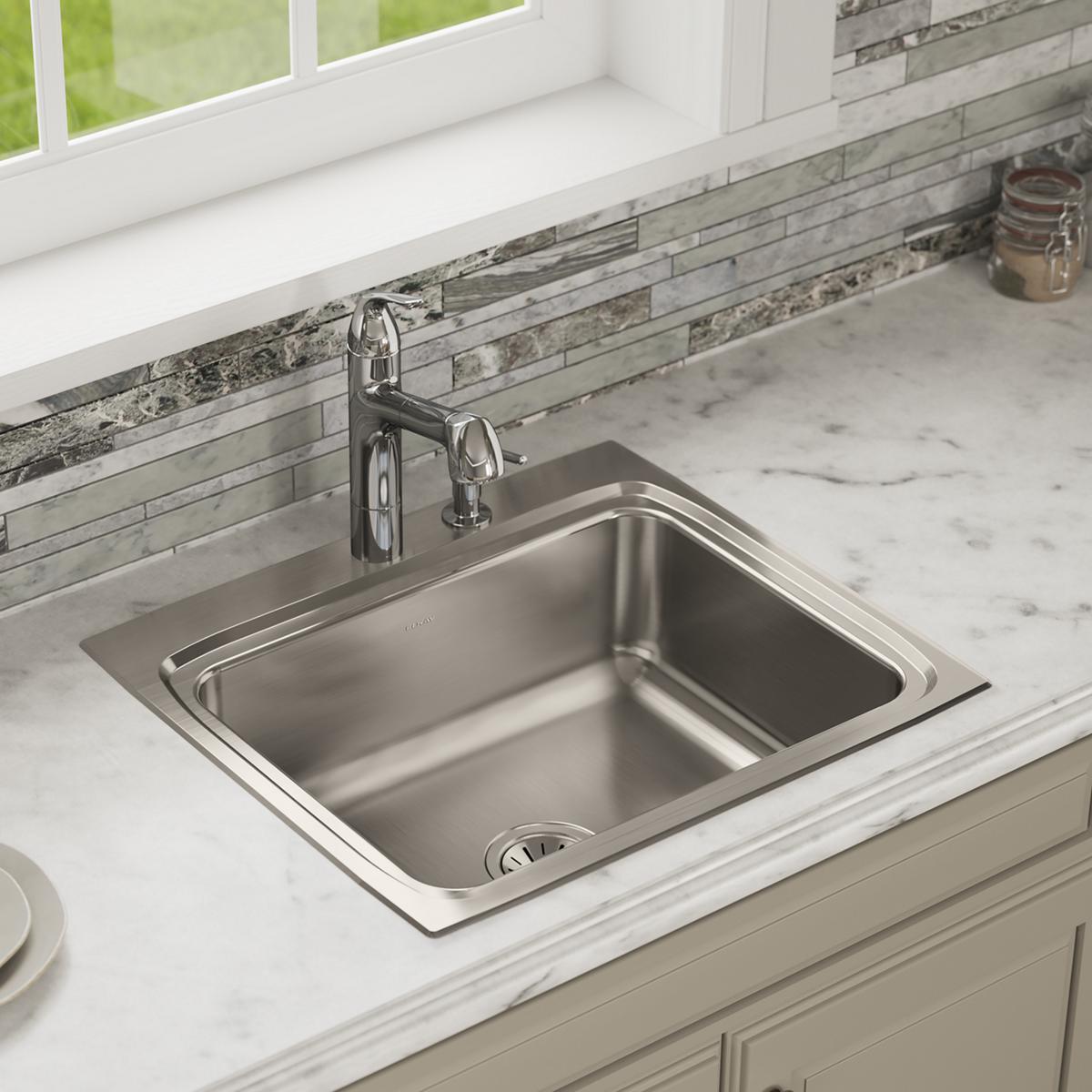 Stainless steel drop-in sink with single bowl installed in marble countertop with chrome faucet and backsplash.