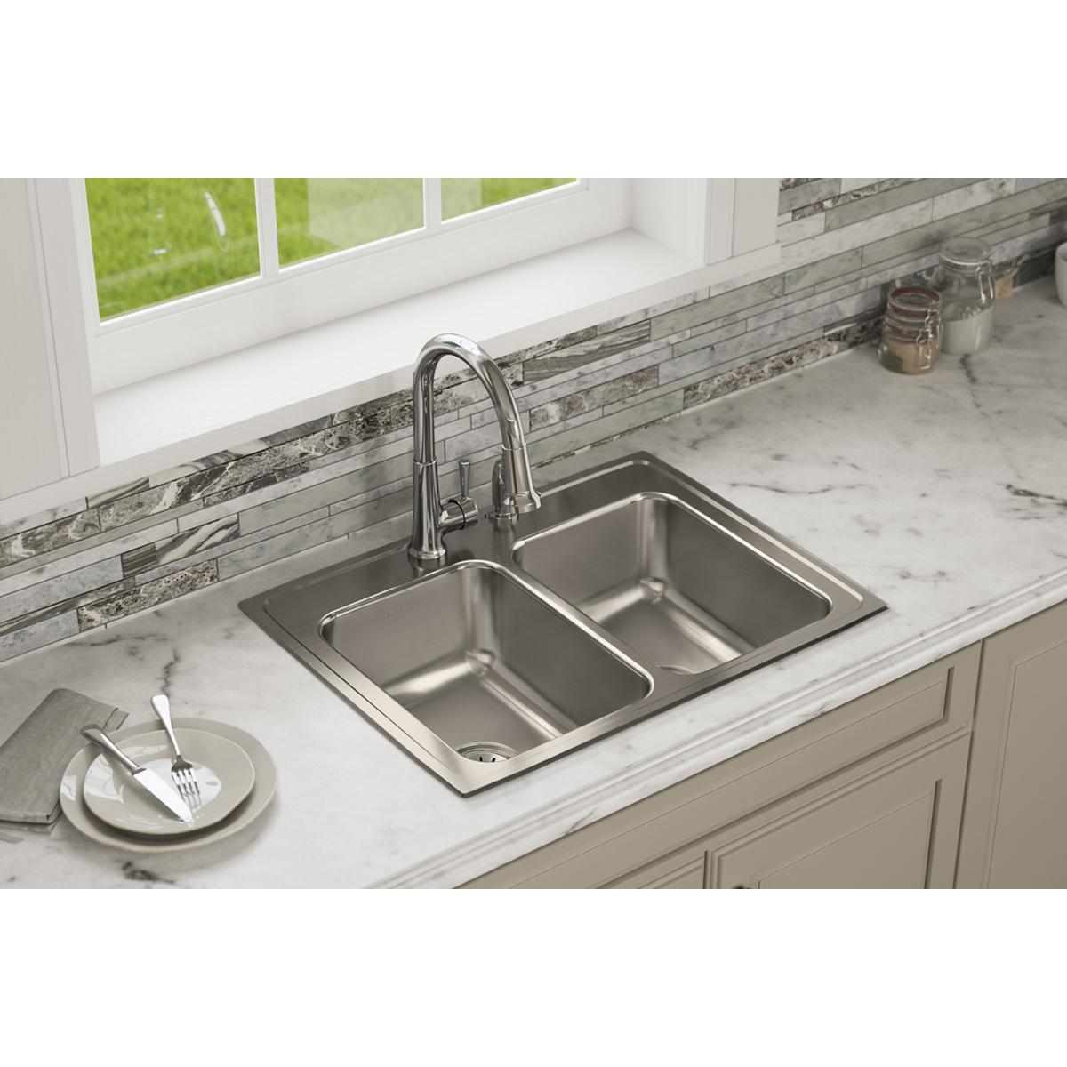 Stainless steel double bowl drop-in sink with two faucet holes installed in white countertop.