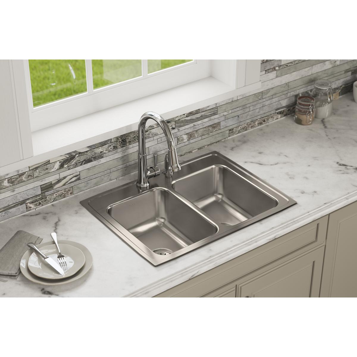 Stainless steel drop-in sink with two equal bowls and chrome pull-down faucet installed in white marble countertop.