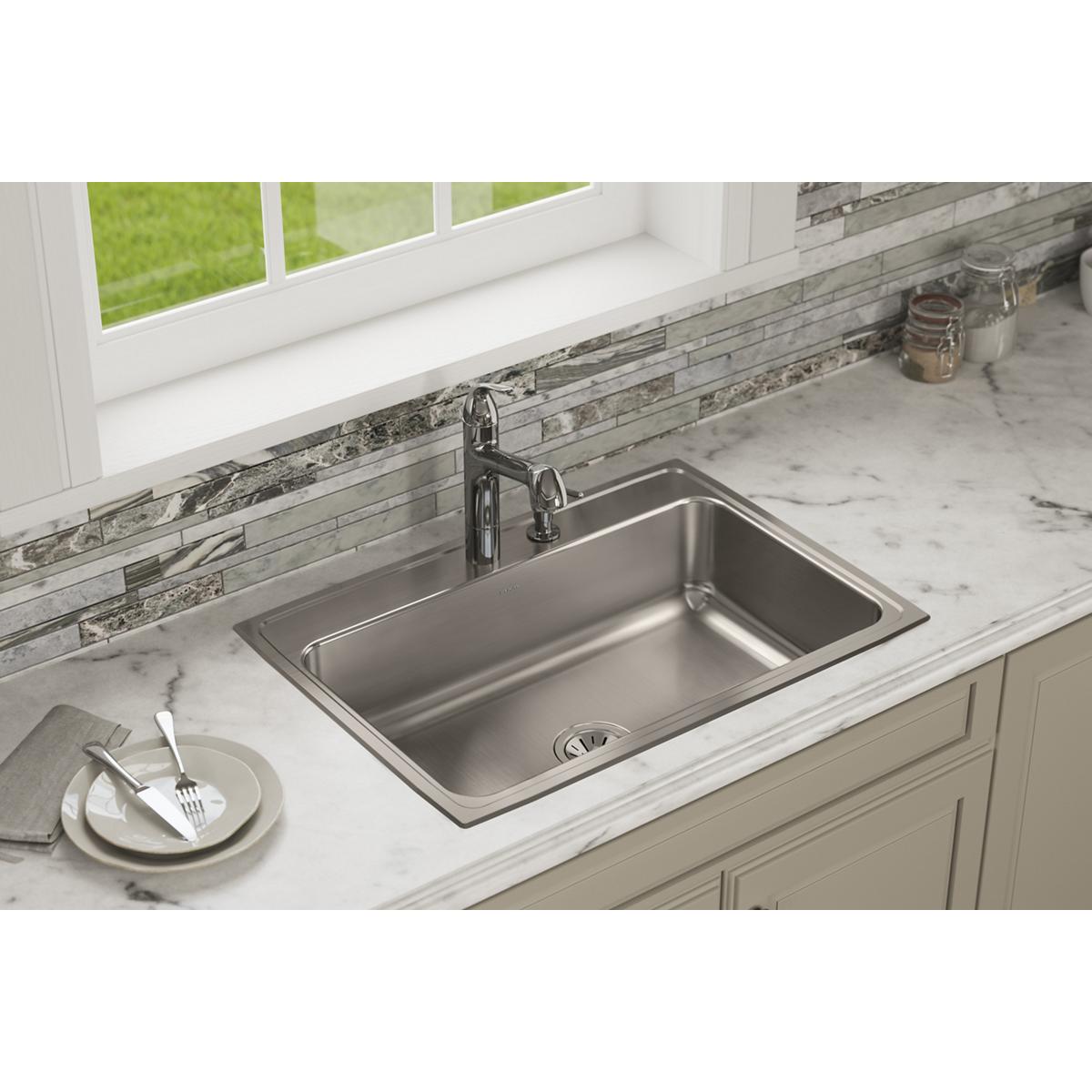 Stainless steel single bowl drop-in sink with two faucet holes installed in white marble countertop.