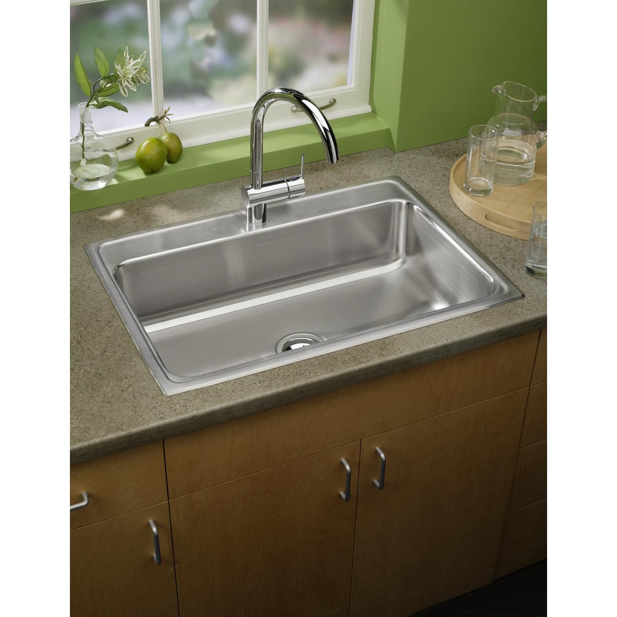 Stainless steel drop-in sink with single bowl and chrome faucet installed in gray countertop with wooden cabinet base.