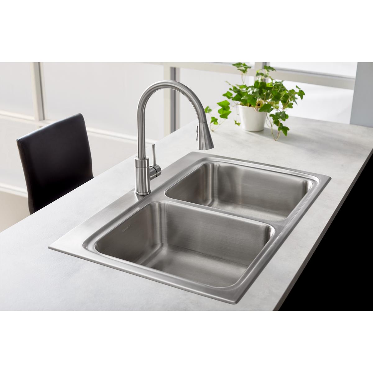 Lustrous steel kitchen faucet with curved spout and pull-down spray mounted above double stainless steel sink.