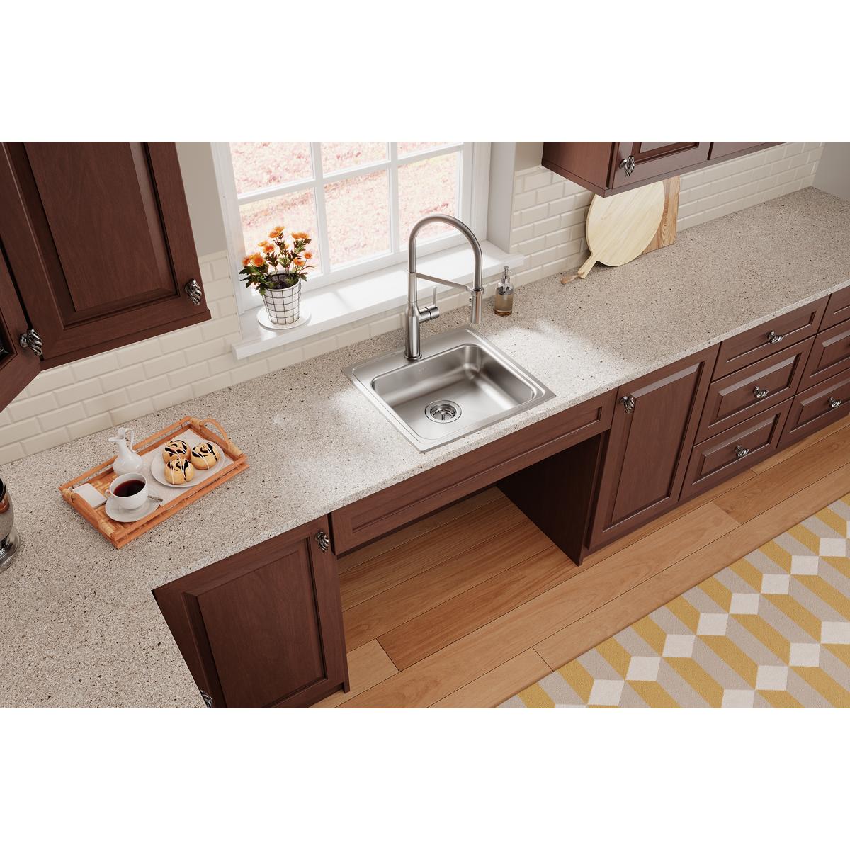 Stainless steel single bowl drop-in sink installed in kitchen countertop with chrome faucet and dark wood cabinetry.