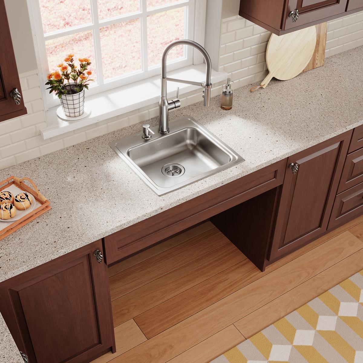 Stainless steel drop-in sink with single bowl and two faucet holes installed in light gray countertop with pull-down faucet.