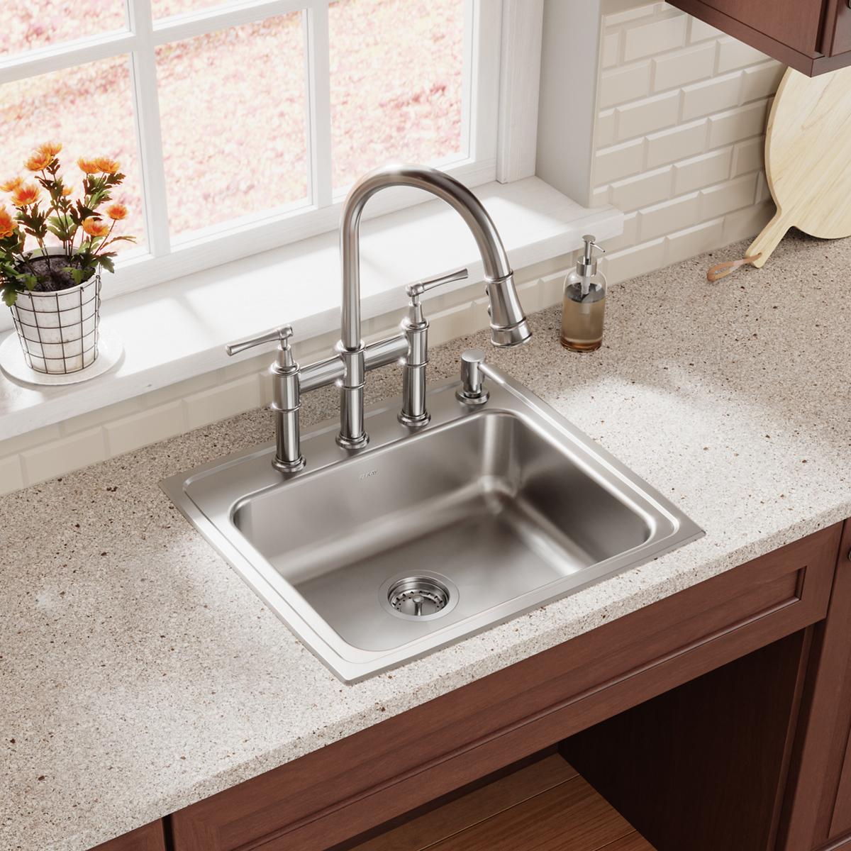 Lustrous steel three-hole bridge faucet with pull-down spray and lever handles installed above stainless steel sink.