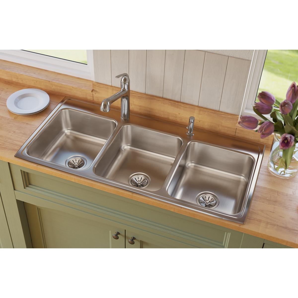 Stainless steel triple bowl drop-in sink with two faucet holes installed in wooden countertop.