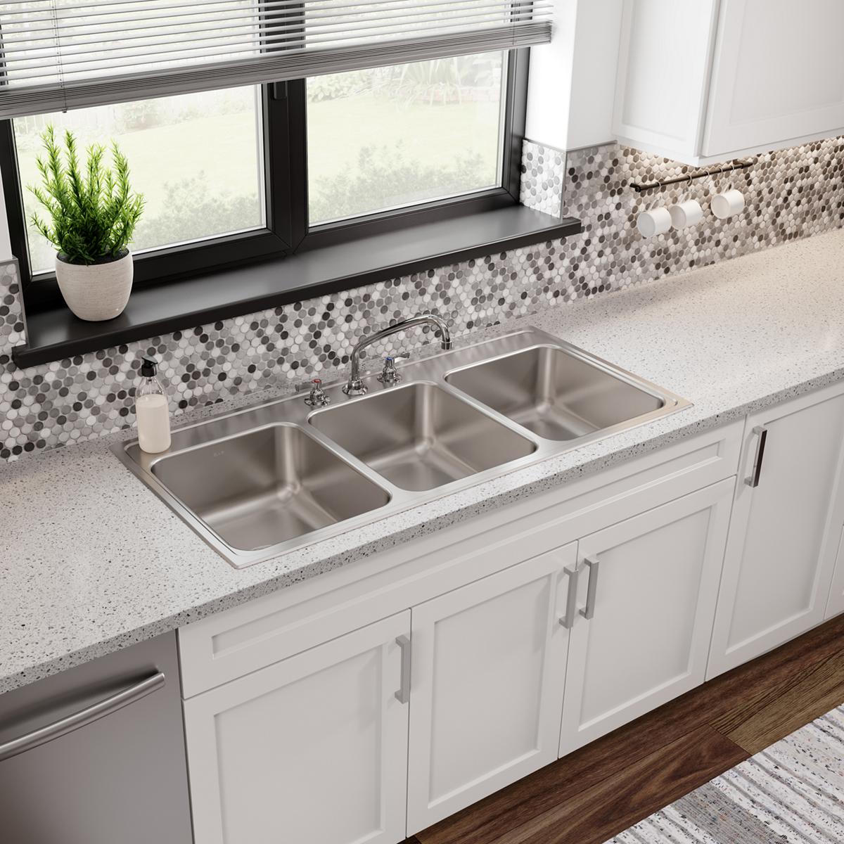 Stainless steel drop-in sink with three equal rectangular bowls and three faucet holes installed in white countertop.