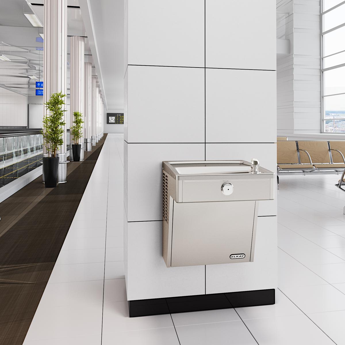 Stainless steel wall-mounted water cooler with filtered dispensing spout installed in modern office hallway.
