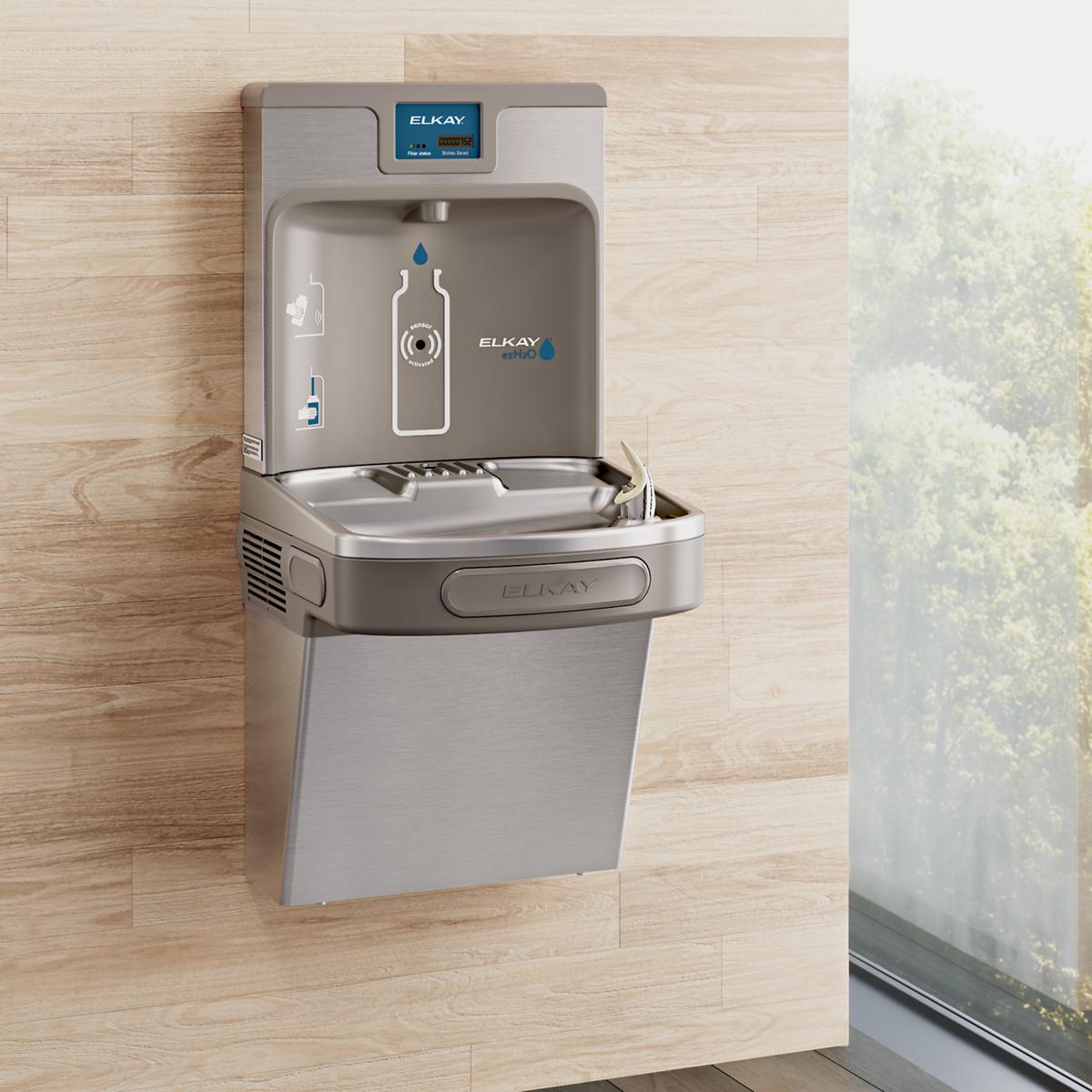 Stainless steel wall-mounted water cooler with bottle filling station, digital display, and lower basin mounted on wooden wal
