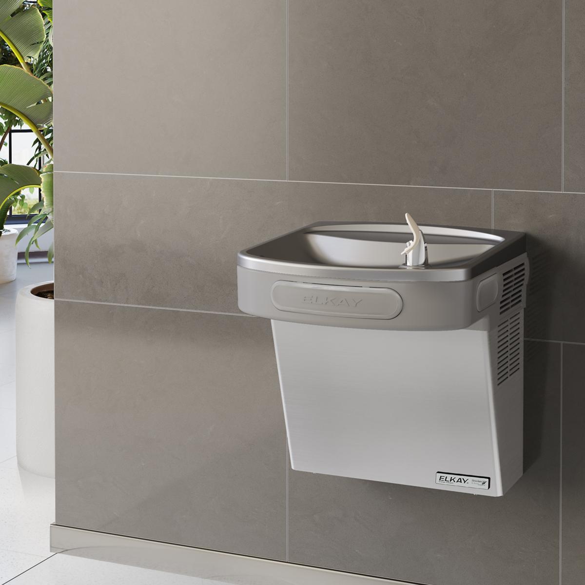 Stainless steel wall-mounted water cooler with filtered refrigerated basin and drinking fountain spout installed on gray tile