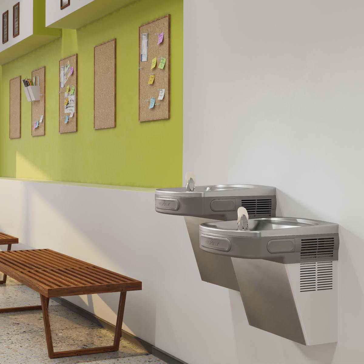 Stainless steel wall-mounted water cooler with two drinking fountains at different heights in an office setting.