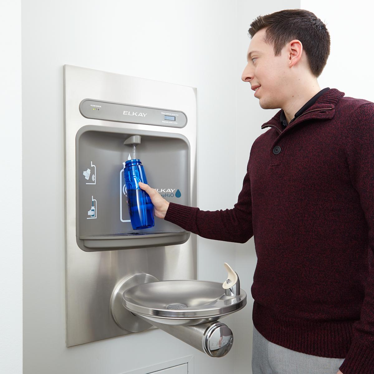 Stainless steel wall-mounted water fountain with bottle filling station and drinking bowl, person filling blue bottle.