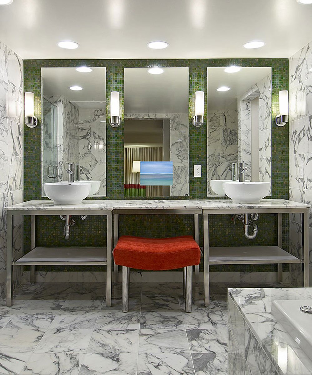 Three illuminated bathroom mirrors with integrated TV screens displaying a beach scene above marble countertops with vessel s