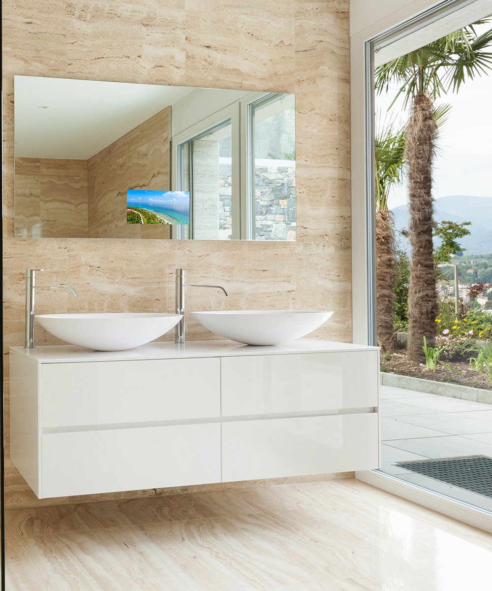 Rectangular illuminated mirror with embedded TV screen displaying landscape image, mounted above dual white vessel sinks in m