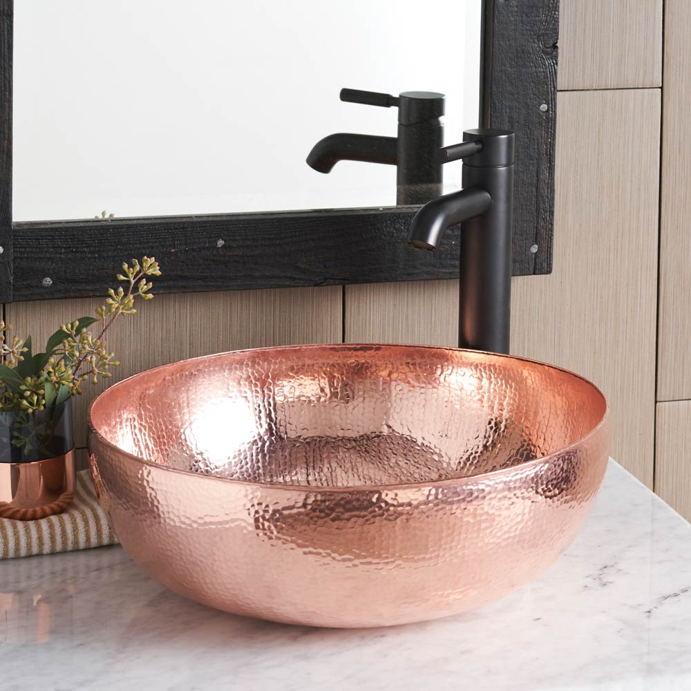 Round copper bathroom sink with hammered texture and oil-rubbed bronze faucet on marble countertop.
