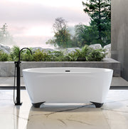 White oval freestanding bathtub with black feet and integrated deck, shown in outdoor bathroom setting with black floor fille