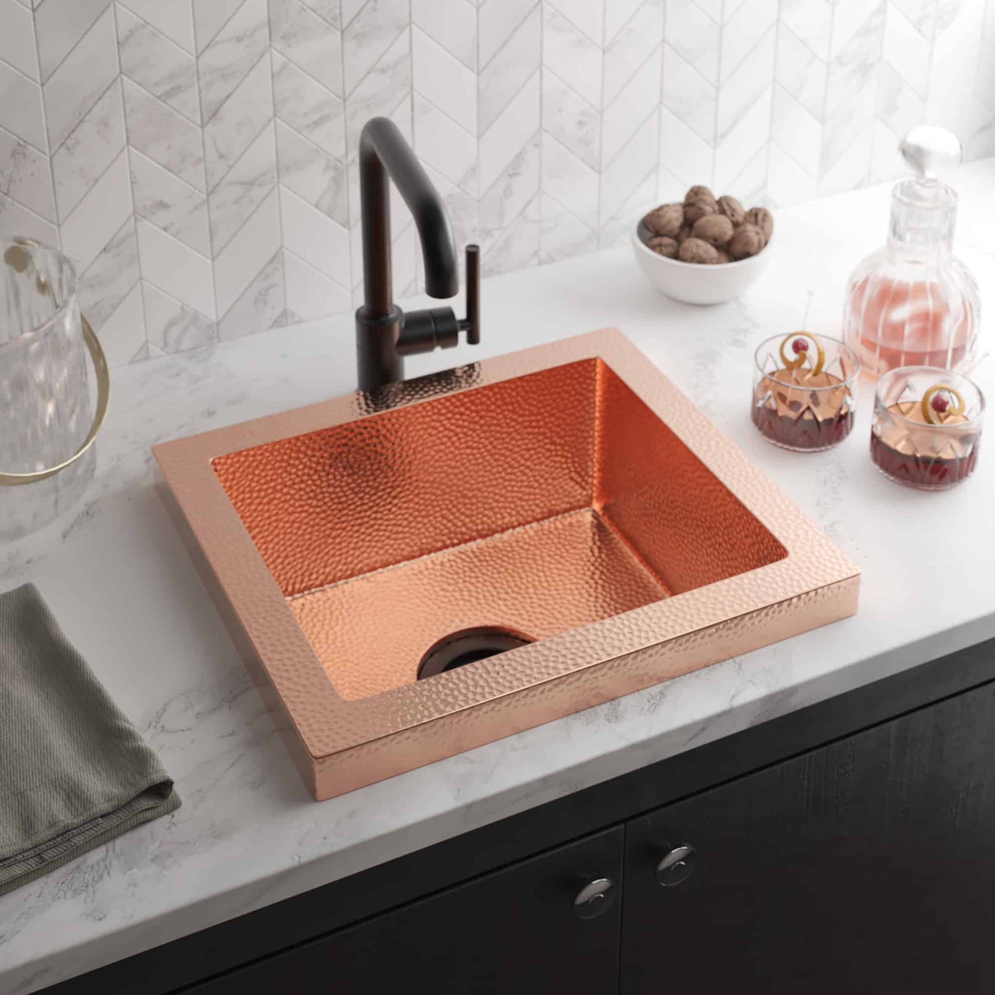 Square polished copper sink with hammered texture finish and black faucet on marble countertop.