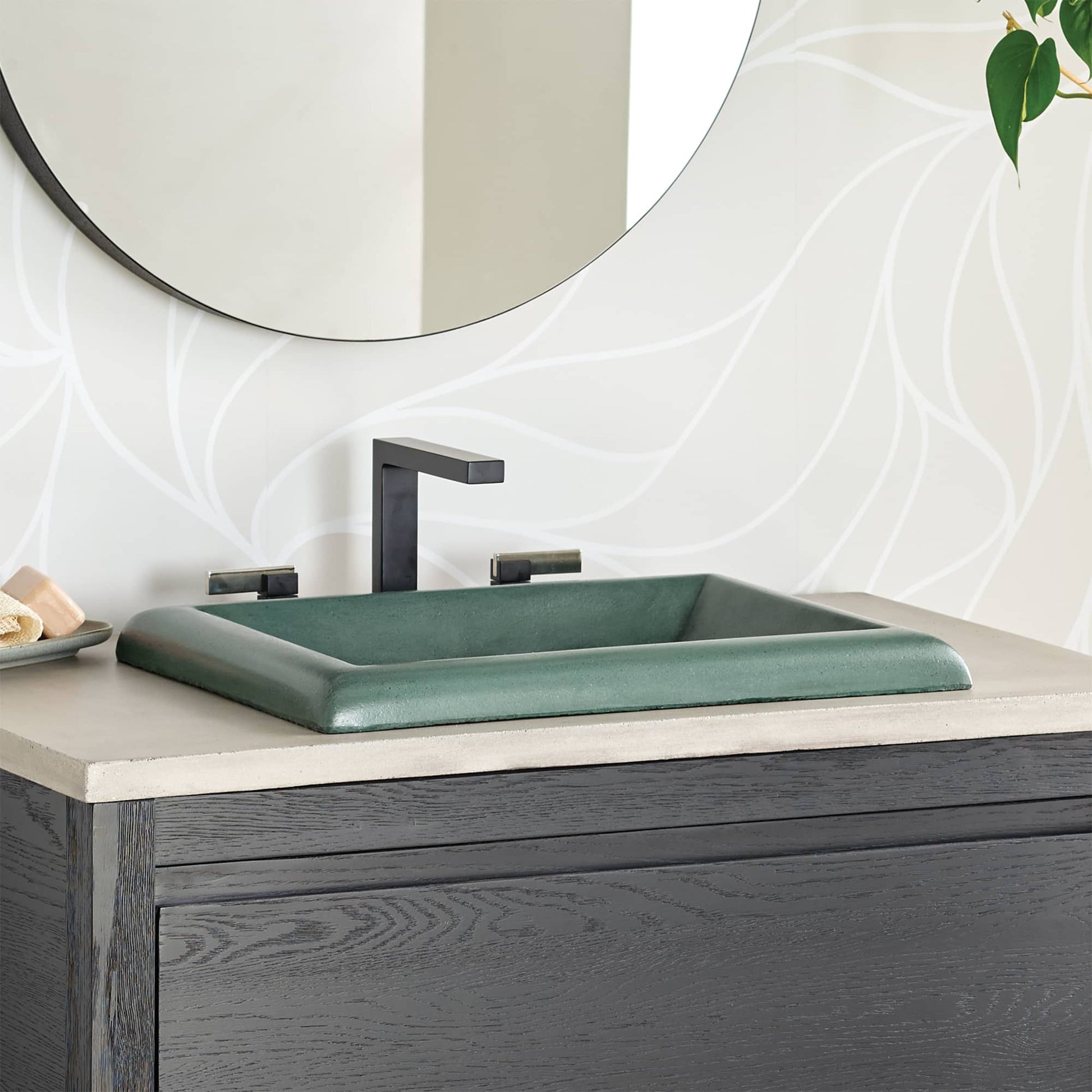 Forest green rectangular vessel sink with curved rim on bathroom vanity with black faucet and round mirror.