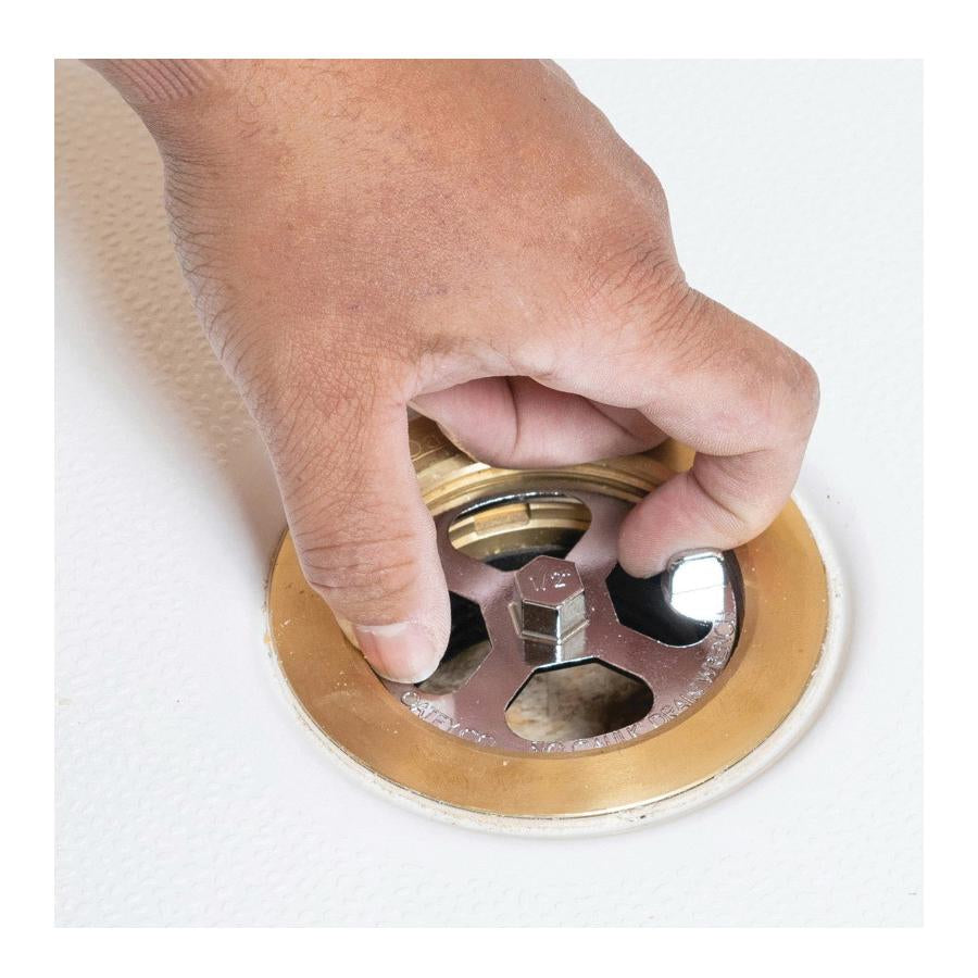 Hand holding brass and plastic shower drain wrench with hexagonal socket over drain opening.