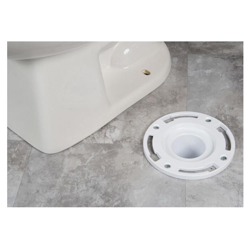 White PVC flange with central opening and mounting holes, displayed next to white toilet base on gray tile floor.