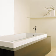 Biscuit-colored rectangular bathtub with chrome faucet in minimalist bathroom setting.