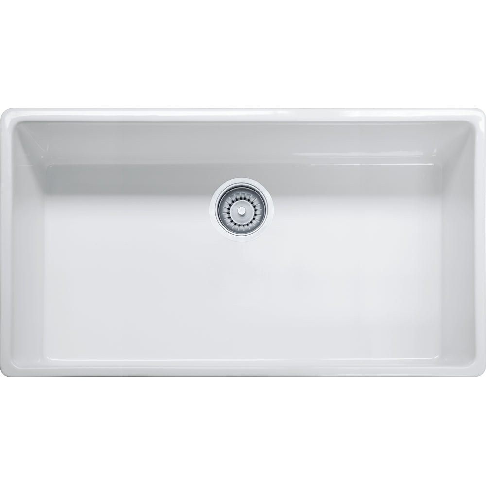 White fireclay farmhouse sink with single bowl and apron front, shown from above with chrome drain fitting.