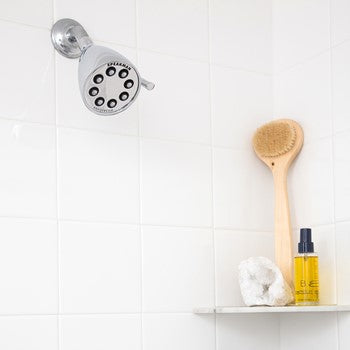 Polished chrome shower head with adjustable spray function mounted on white tile wall above shelf.