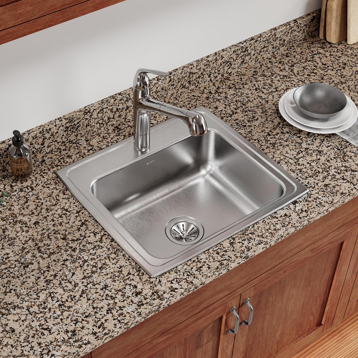 Stainless steel single bowl drop-in sink with one faucet hole, mounted in speckled granite countertop with wood cabinet base.