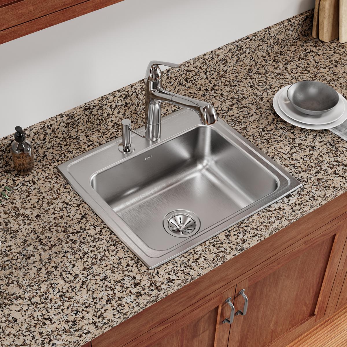 Stainless steel drop-in sink with single bowl and two faucet holes installed in speckled granite countertop with chrome fauce