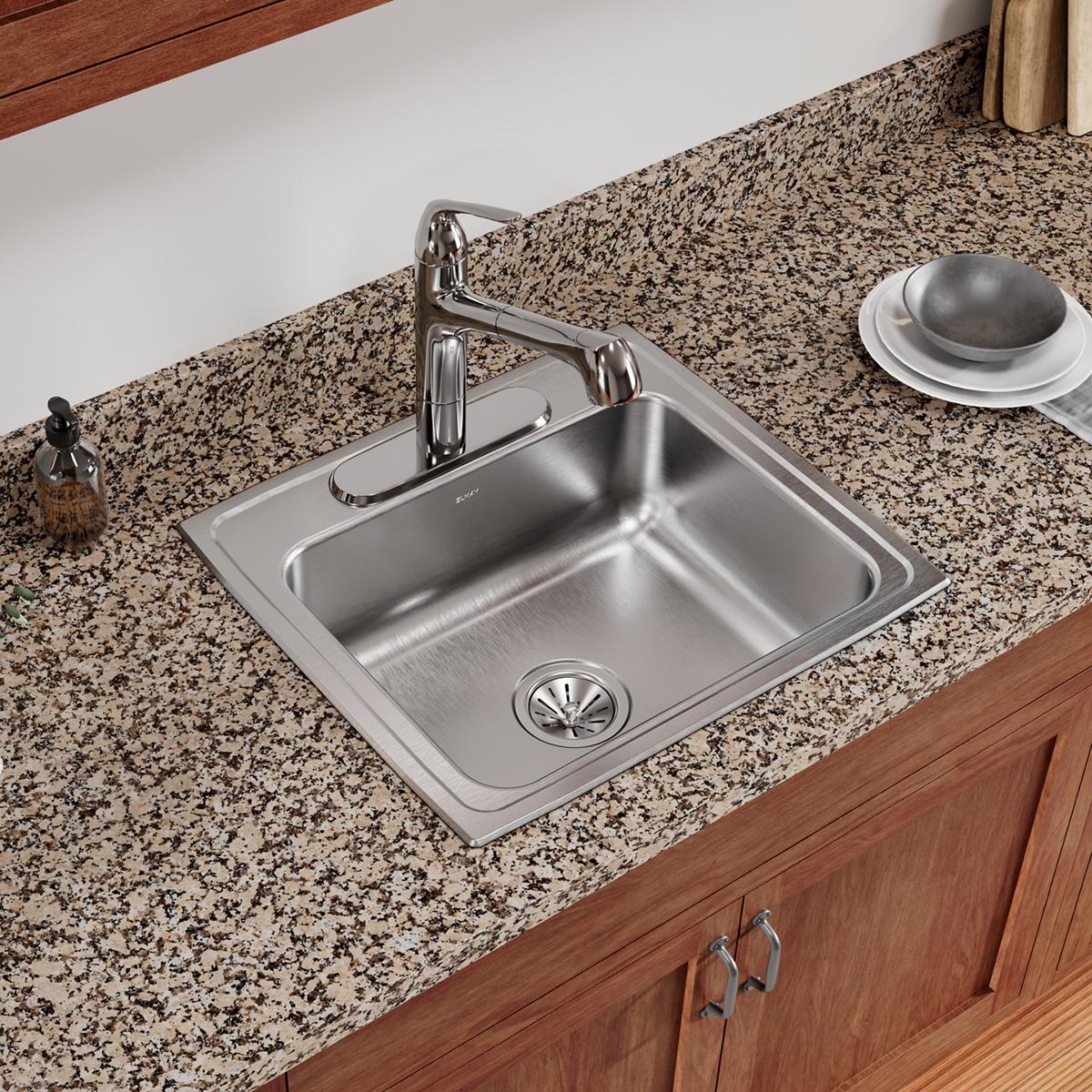 Stainless steel drop-in sink with single bowl, chrome faucet, and drain strainer installed in speckled granite countertop.