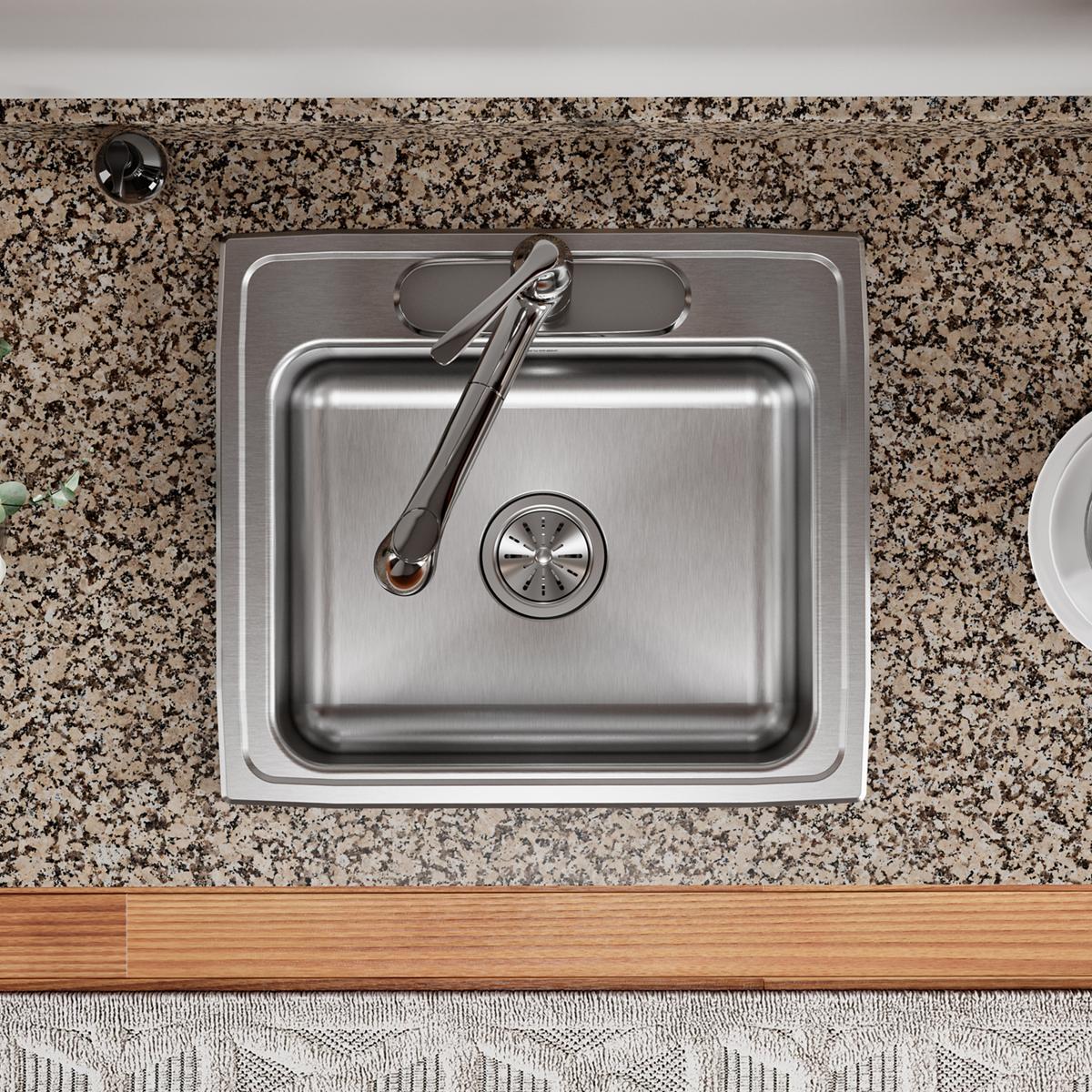 Stainless steel single bowl drop-in sink with faucet and drain strainer installed in speckled granite countertop.