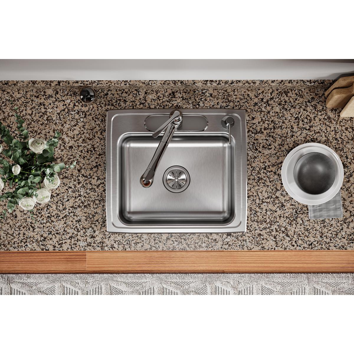 Stainless steel drop-in sink with single bowl and faucet installed in speckled granite countertop.