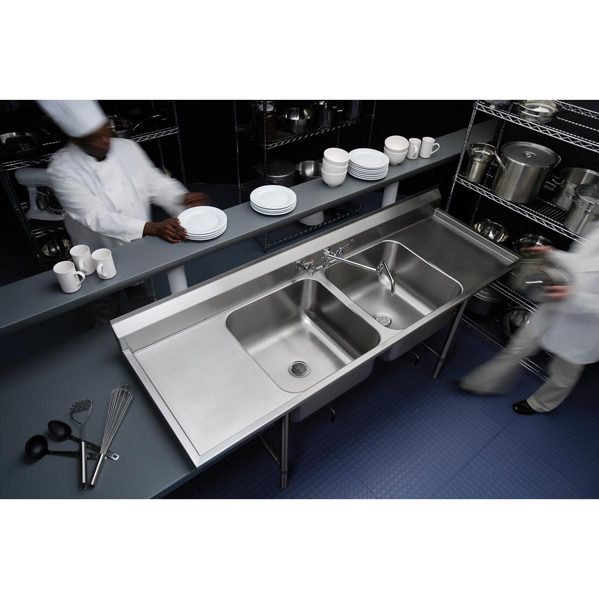 Stainless steel double compartment sink with left and right drainboards, two faucets, and floor-mounted legs in a commercial 