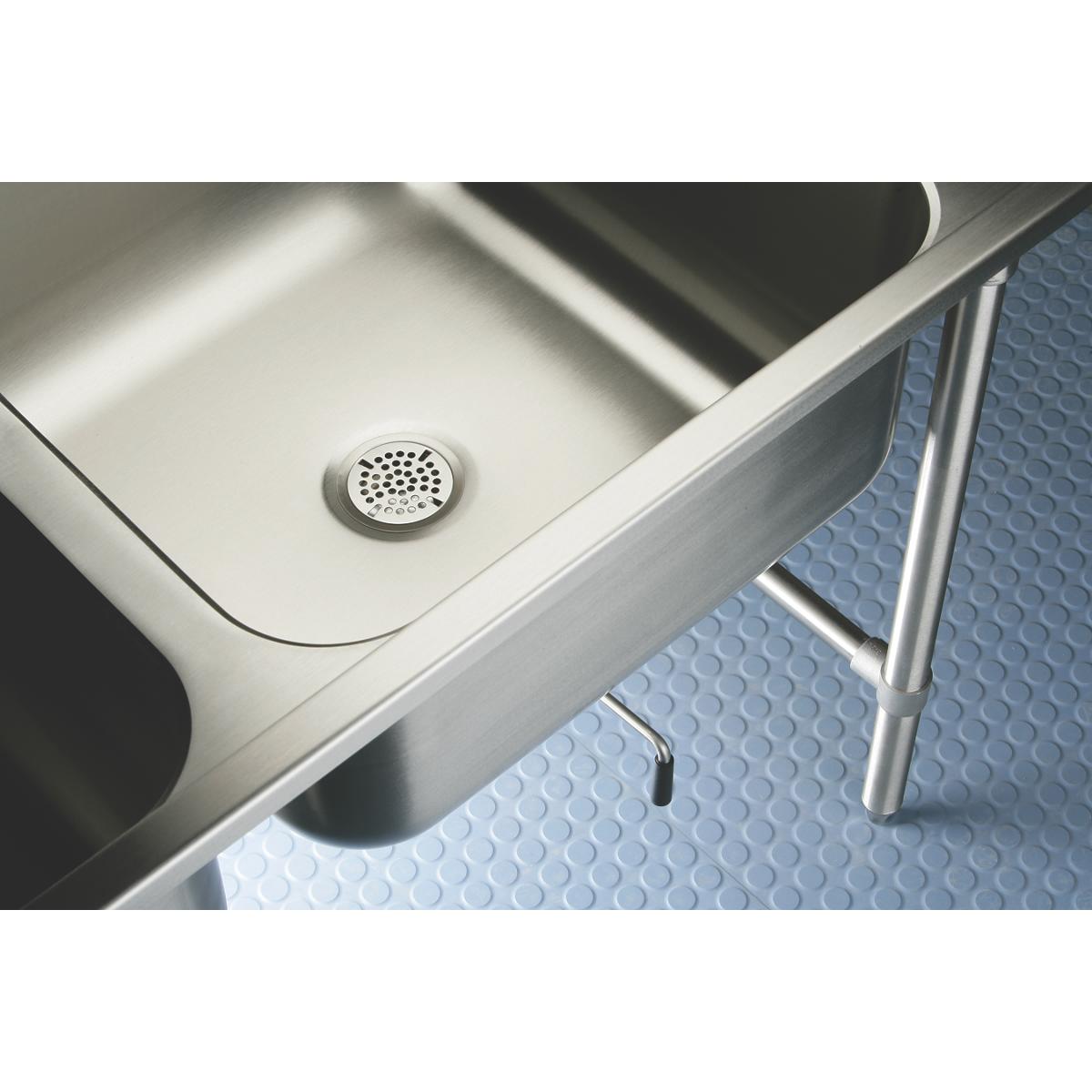 Stainless steel double compartment sink with drain holes and metal legs on textured floor surface.