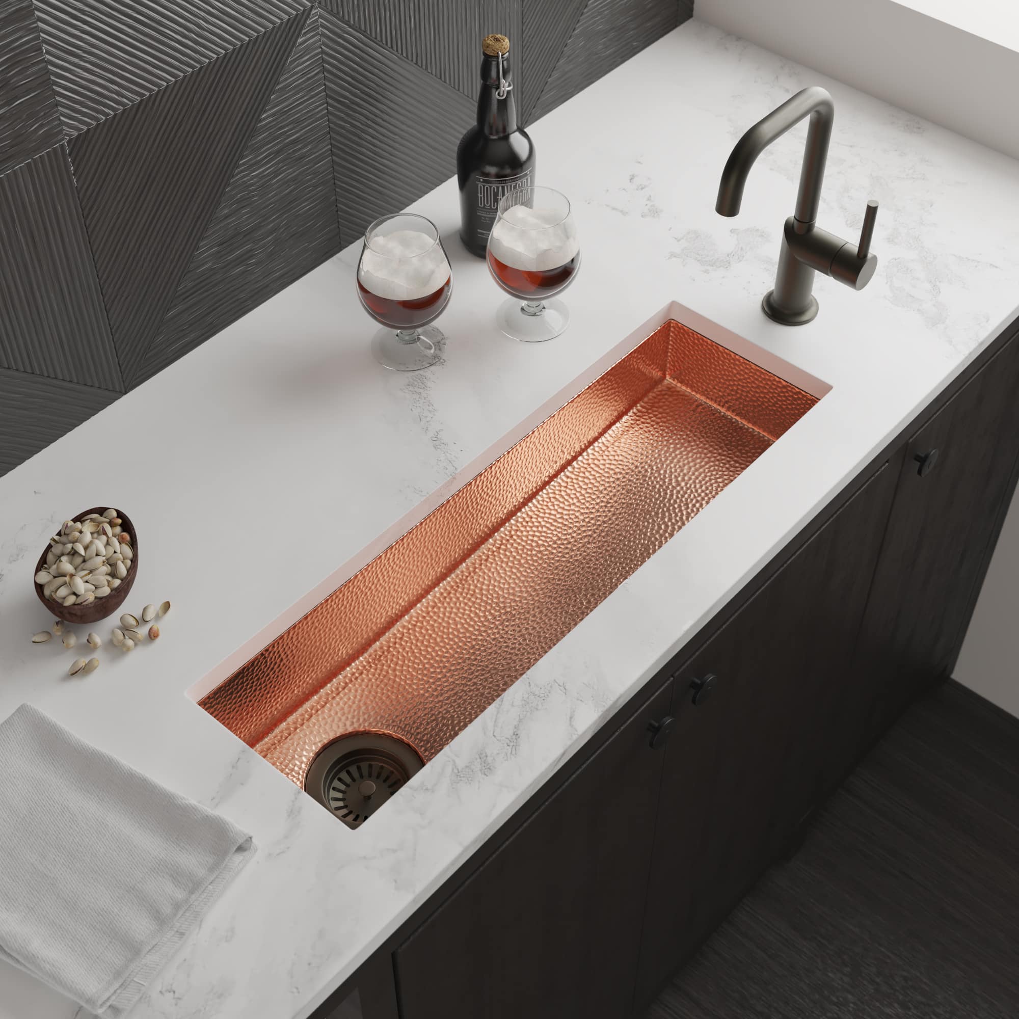 Polished copper rectangular sink with hammered texture installed in white marble countertop with dark faucet.