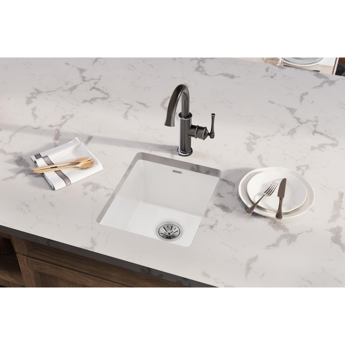 White fireclay single bowl undermount bar sink installed in marble countertop with faucet.
