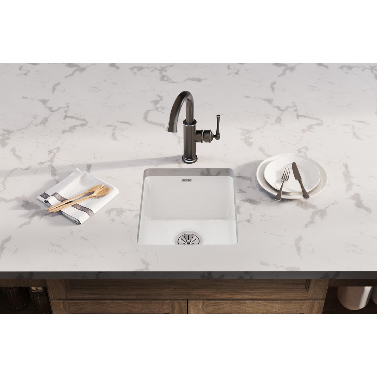 White fireclay undermount bar sink with single bowl and black faucet installed in marble countertop.