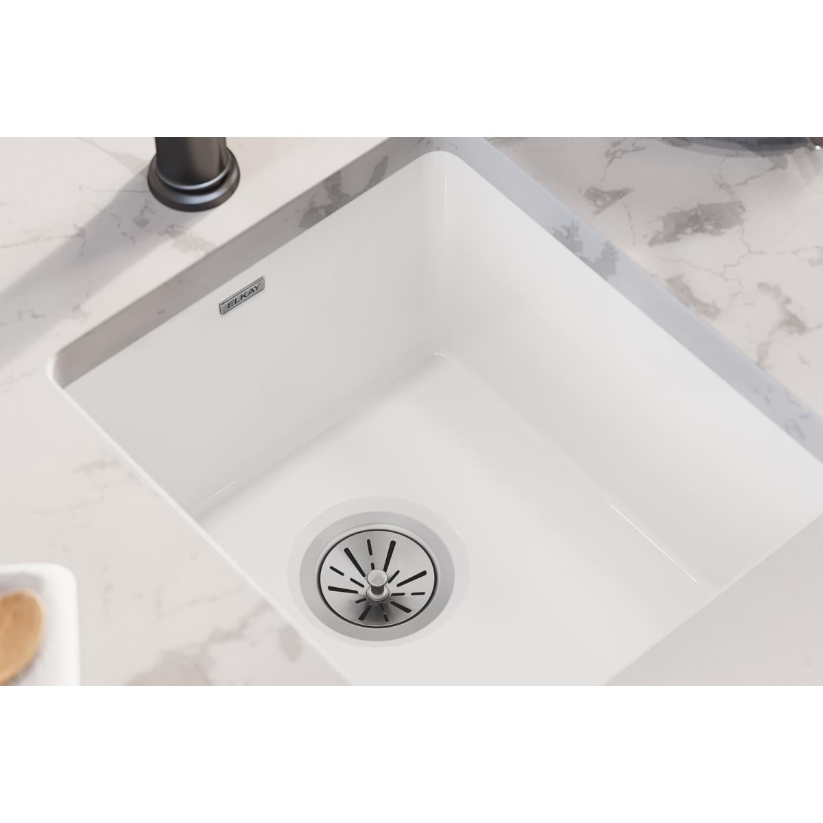 White fireclay undermount bar sink with single bowl and drain strainer, installed below marble countertop.